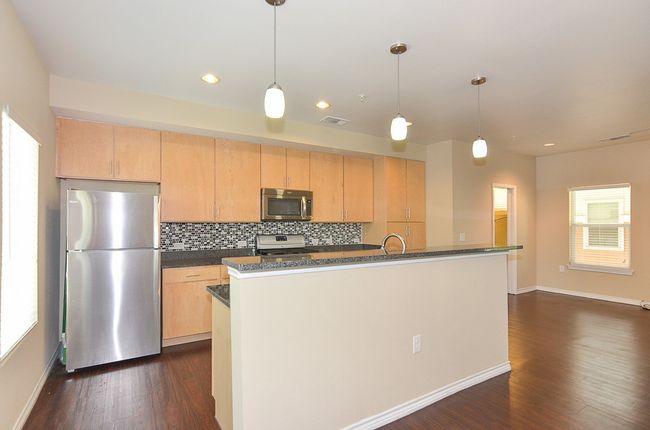 Kitchen featuring baseboards, backsplash, visible vents, dark wood finished floors, and appliances with stainless steel finishes | Image 7