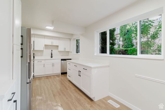 Kitchen with a sink, white cabinets, stainless steel dishwasher, visible vents, and light wood-style floors | Image 4