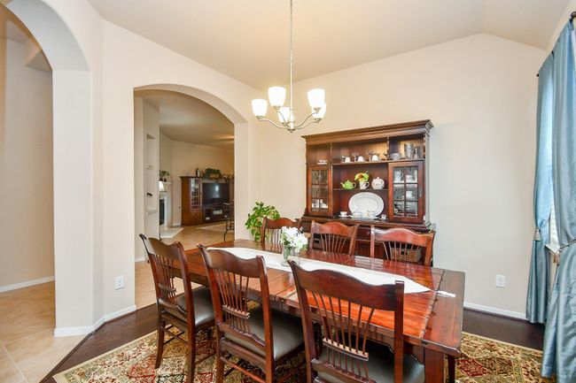 This dining room features elegant wood furniture, a classic china cabinet, and a warm chandelier. The arched doorway leads to a cozy living area, creating an inviting flow between spaces. | Image 5