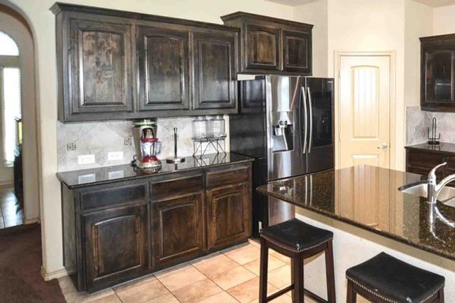 Kitchen with stainless steel fridge, tasteful backsplash, dark stone counters, light tile patterned flooring, and a kitchen bar | Image 5