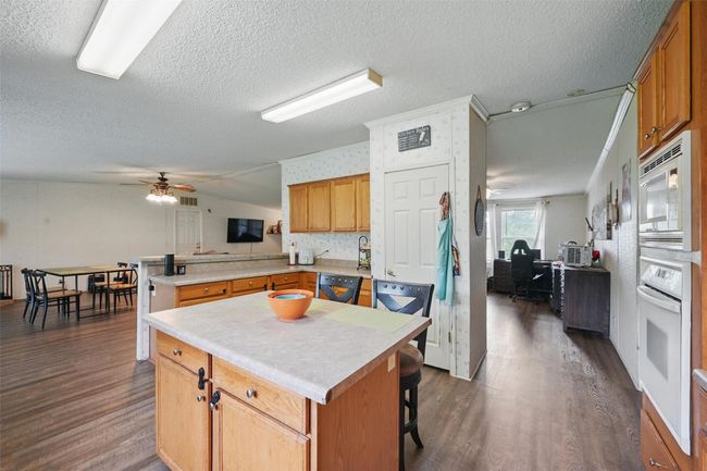 Kitchen with white appliances, a peninsula, dark wood finished floors, a ceiling fan, and a textured ceiling | Image 8