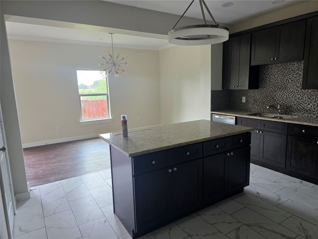 Kitchen with light marble finish floors, a sink, a chandelier, light stone counters, and crown molding | Image 9