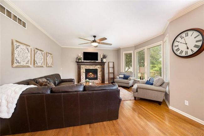 Living area with ceiling fan, light wood finished floors, ornamental molding, a fireplace, and baseboards | Image 8