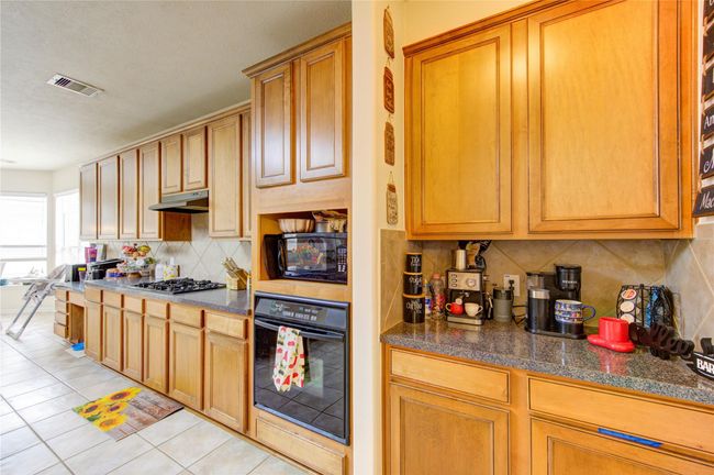 This kitchen features ample wood cabinetry, a built-in oven, and a gas cooktop. The countertops offer plenty of workspace, and there's a cozy breakfast nook area with large windows for natural light. The tile flooring adds a practical touch. | Image 14