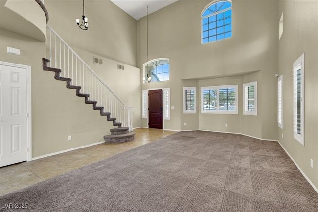 Entrance foyer featuring a towering ceiling, carpet, a chandelier, tile patterned flooring, and stairs | Image 6