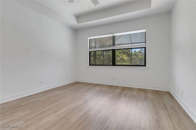 Empty room featuring a raised ceiling, light wood-type flooring, baseboards, and a ceiling fan | Image 17
