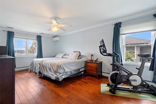 Bedroom with crown molding, dark wood-type flooring, a baseboard heating unit, ceiling fan, and a wall mounted AC | Image 17