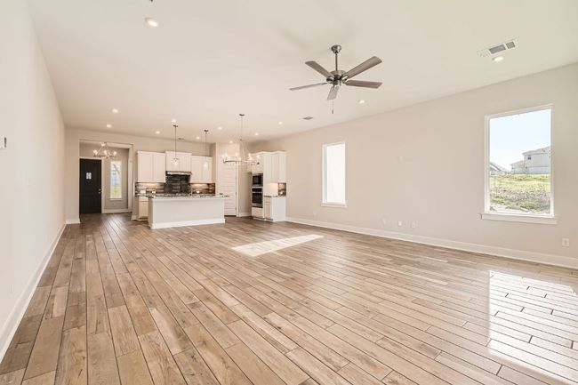 Unfurnished living room with light wood-style floors, visible vents, baseboards, and ceiling fan with notable chandelier | Image 8