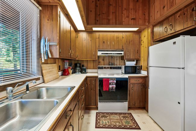 Kitchen with white appliances, under cabinet range hood, light countertops, and wooden cabinets | Image 18