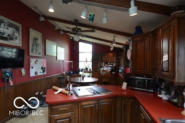 kitchen featuring stainless steel microwave, ceiling fan, vaulted ceiling with beams, a wainscoted wall, and a peninsula | Image 11