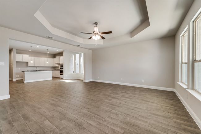 Unfurnished living room with ceiling fan, a tray ceiling, light hardwood / wood-style floors, and a wealth of natural light | Image 6