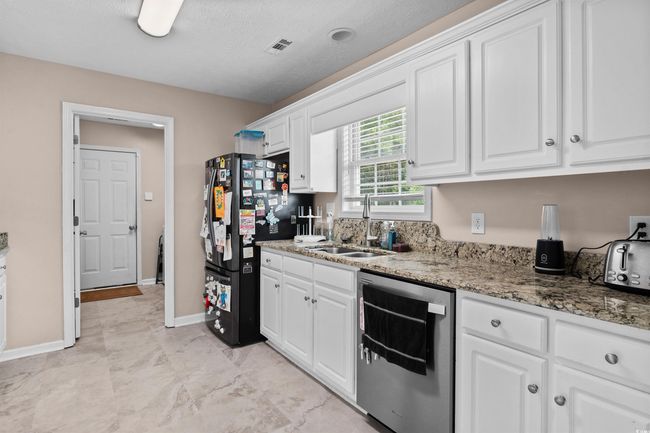 Kitchen featuring dishwasher, freestanding refrigerator, white cabinets, and light stone countertops | Image 5