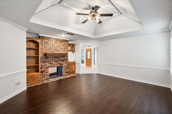 Unfurnished living room with a tray ceiling, a ceiling fan, dark wood finished floors, crown molding, and baseboards | Image 6