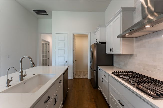 Kitchen featuring wall chimney exhaust hood, stainless steel appliances, backsplash, dark wood-style floors, and light stone counters | Image 15