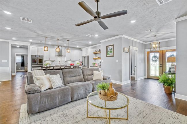 Living room featuring ceiling fan with notable chandelier, wood-type flooring, sink, crown molding, and a textured ceiling | Image 13