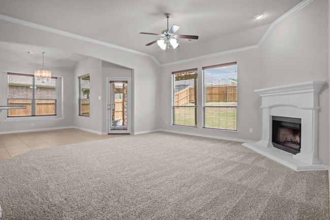 Unfurnished living room with ornamental molding, baseboards, light colored carpet, a fireplace with raised hearth, and ceiling fan with notable chandelier | Image 11
