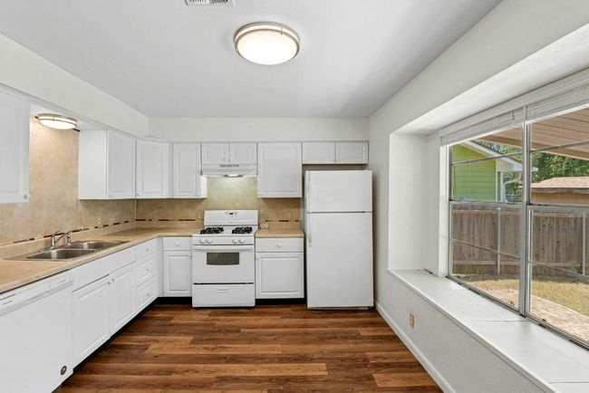 Kitchen with white appliances, light countertops, white cabinetry, backsplash, and dark wood-type flooring | Image 8
