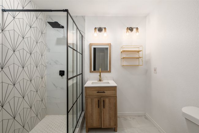 Full bath featuring marble look tile flooring, vanity, a stall shower, and toilet | Image 12