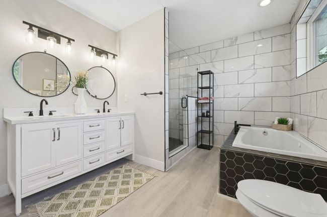 Full bathroom featuring wood finished floors, a bath, double vanity, a stall shower, and toilet | Image 22