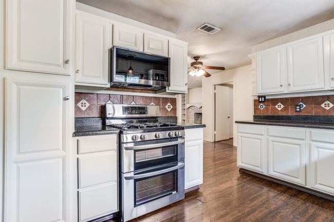 Kitchen featuring appliances with stainless steel finishes, dark countertops, white cabinets, decorative backsplash, and ceiling fan | Image 13