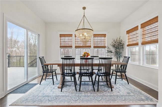 Bright and spacious breakfast area surrounded by large windows with natural woven shades, offering scenic views and abundant sunlight. Features include a stylish chandelier and sliding glass doors that open to the back deck, perfect for indoor-outdoor entertaining. | Image 17