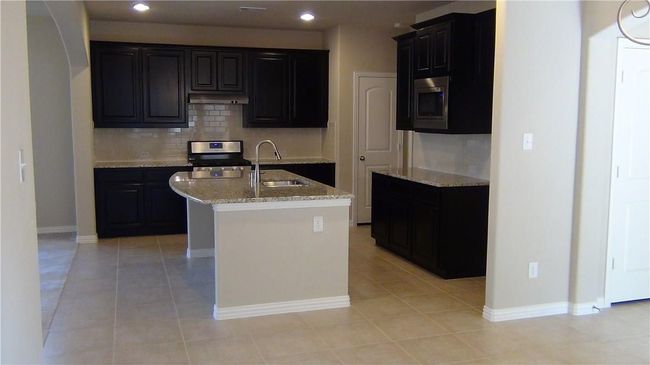Kitchen with a sink, appliances with stainless steel finishes, under cabinet range hood, decorative backsplash, and light stone counters | Image 6
