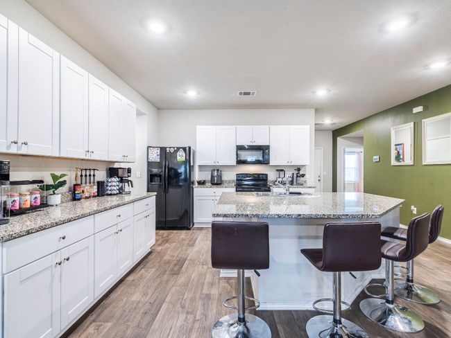 Kitchen featuring white cabinetry, a kitchen bar, visible vents, black appliances, and light wood-style floors | Image 8