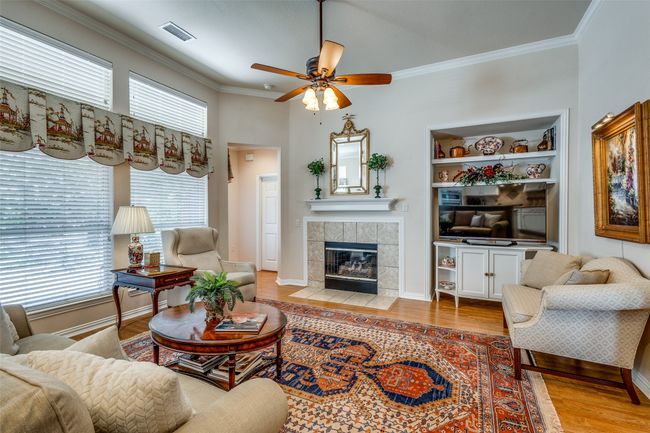 Living area featuring ornamental molding, light wood-type flooring, ceiling fan, a tile fireplace, and built in features | Image 7
