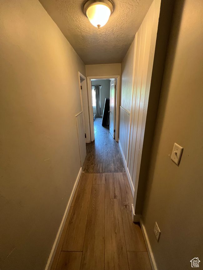 Hall featuring a textured ceiling, wood finished floors, and baseboards | Image 9