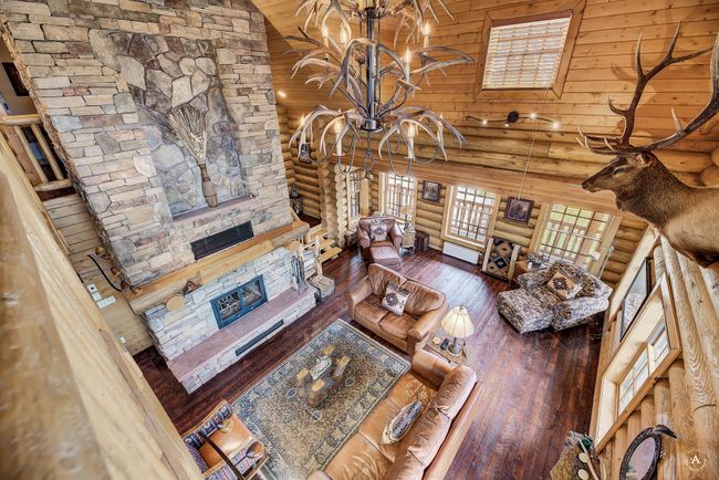 Living room featuring a stone fireplace, rustic walls, hardwood / wood-style floors, high vaulted ceiling, and a chandelier | Image 33