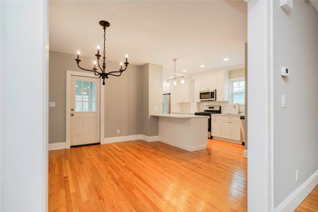 Kitchen with a notable chandelier, a peninsula, white cabinetry, light wood-style floors, and stainless steel appliances | Image 13
