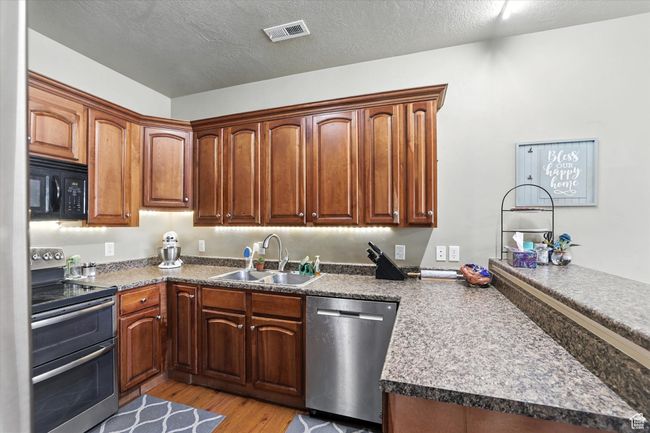 Kitchen with stainless steel appliances, a peninsula, light wood-style floors, a textured ceiling, and dark countertops | Image 12
