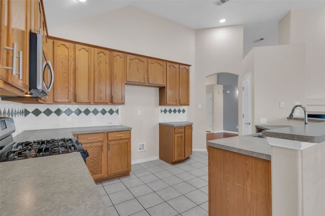 Kitchen featuring appliances with stainless steel finishes, arched walkways, backsplash, light tile patterned floors, and high vaulted ceiling | Image 9