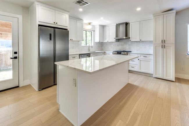 Kitchen featuring appliances with stainless steel finishes, light wood-type flooring, a sink, visible vents, and wall chimney exhaust hood | Image 12