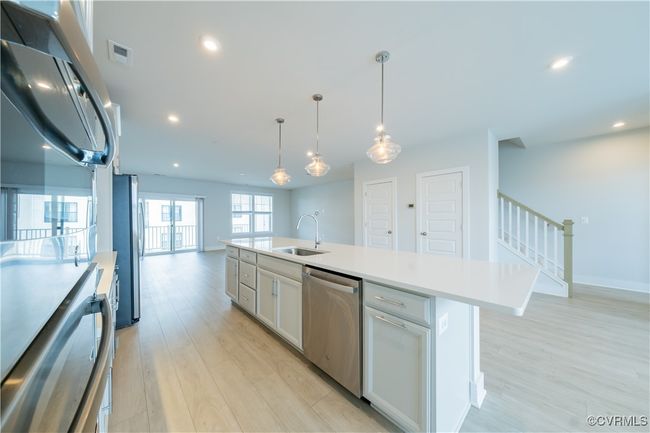 Kitchen featuring stainless steel appliances, a sink, light wood-type flooring, open floor plan, and light countertops | Image 15