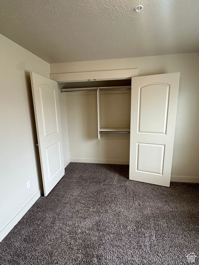 Unfurnished bedroom with a textured ceiling, a closet, dark carpet, and baseboards | Image 15