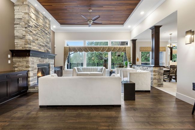Living room with decorative columns, wooden ceiling, ornamental molding, dark wood-style flooring, and a tray ceiling | Image 6