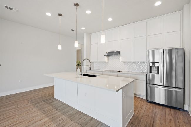 Kitchen with stainless steel refrigerator with ice dispenser, backsplash, light wood-type flooring, white cabinetry, and recessed lighting | Image 8