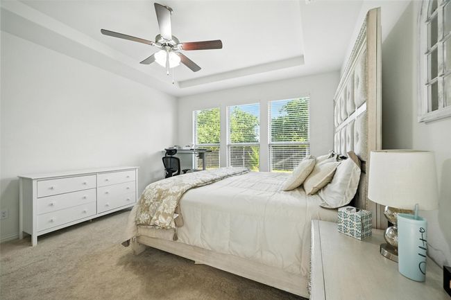 Carpeted bedroom with a raised ceiling, a ceiling fan, and an office area | Image 18