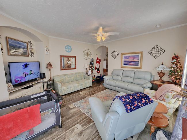 Living room with a textured ceiling, ceiling fan, light wood-type flooring, and ornamental molding | Image 6