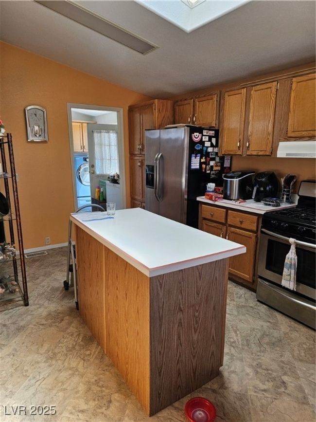 Kitchen with a kitchen island, stainless steel fridge, brown cabinetry, range, and extractor fan | Image 26
