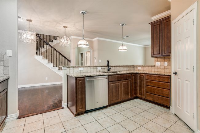 Kitchen featuring dishwasher, a sink, light tile patterned floors, a peninsula, and a chandelier | Image 4