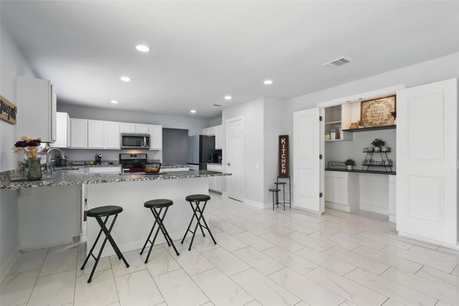 Kitchen featuring stainless steel appliances, a kitchen breakfast bar, recessed lighting, dark stone counters, and white cabinets | Image 7