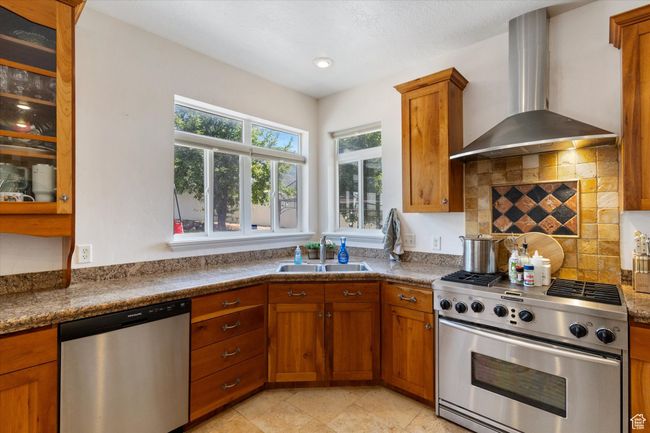 Kitchen featuring appliances with stainless steel finishes, wall chimney exhaust hood, brown cabinets, decorative backsplash, and recessed lighting | Image 6