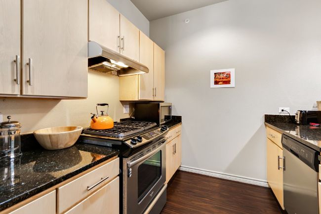 Kitchen with stainless steel appliances, under cabinet range hood, dark wood-style floors, and dark stone counters | Image 16