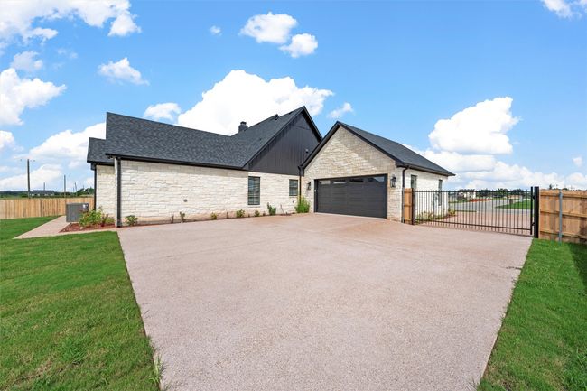 View of front of house featuring stone siding, concrete driveway, roof with shingles, a gate, and an attached garage | Image 33