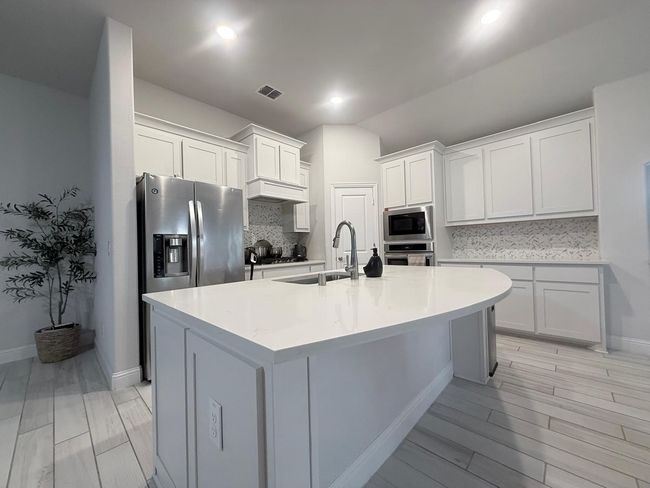 Kitchen with appliances with stainless steel finishes, tasteful backsplash, white cabinetry, a kitchen island with sink, and light wood-style floors | Image 8