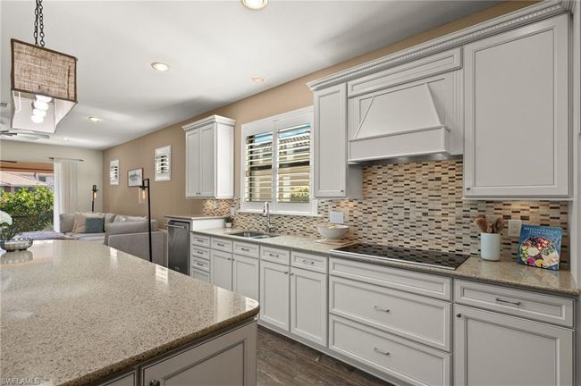 Kitchen featuring custom exhaust hood, black electric stovetop, sink, tasteful backsplash, and light stone counters | Image 11