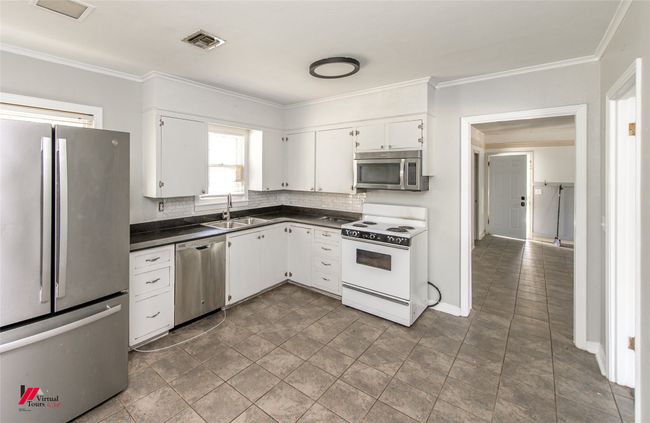 Kitchen featuring visible vents, stainless steel appliances, dark countertops, white cabinetry, and a sink | Image 11