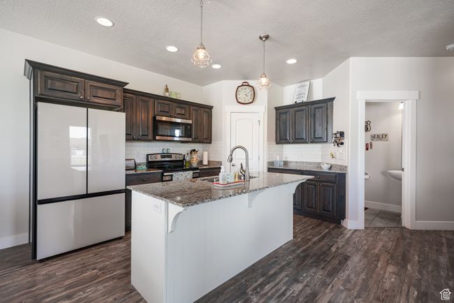 Kitchen featuring appliances with stainless steel finishes, dark stone countertops, a kitchen bar, tasteful backsplash, and dark brown cabinets | Image 8